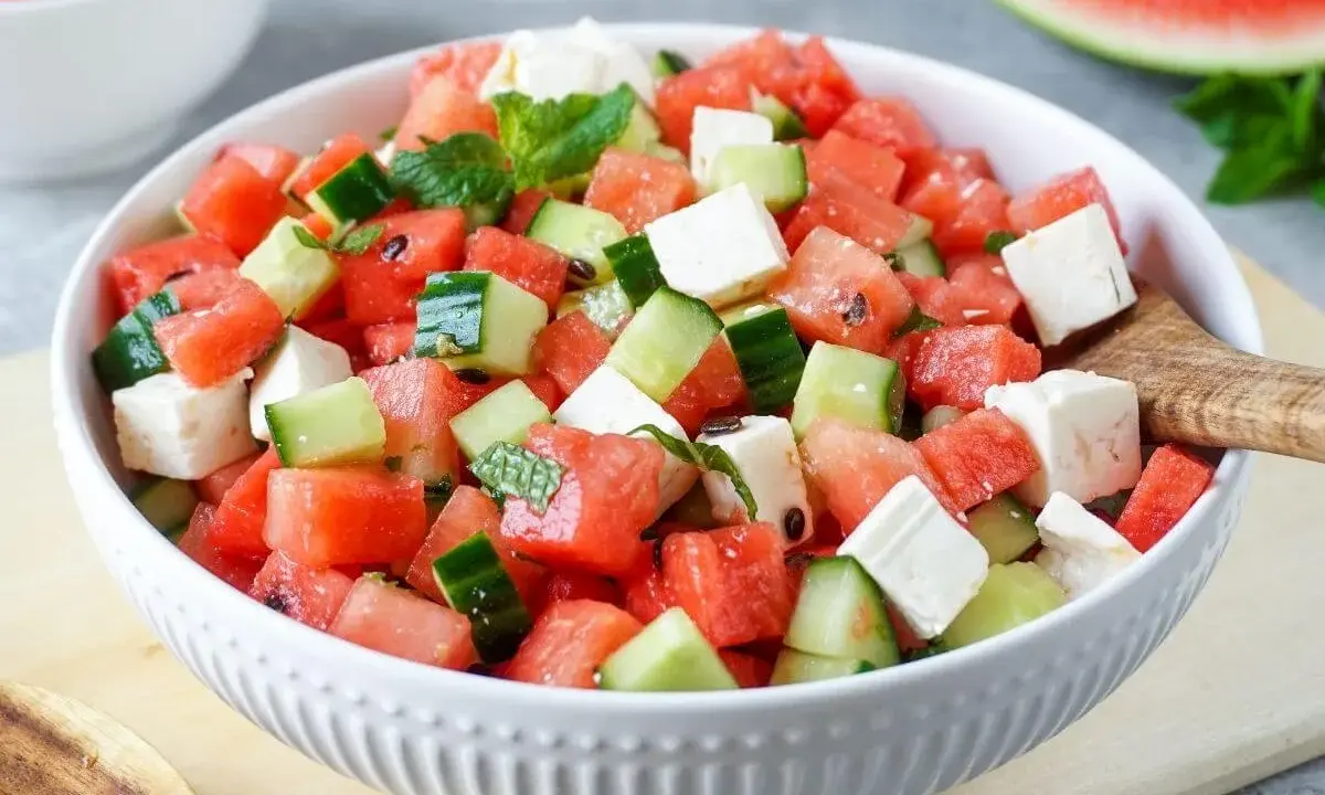 Erfrischender melonen feta salat mit Gurken und Minze in einer weißen Schüssel, bereit zum Servieren.