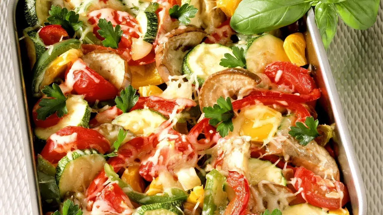 Buntes Ofengemüse mit geschmolzenem Käse, ein köstliches Gericht für low carb rezepte. Frische Kräuter garnieren die Zucchini, Paprika und Tomaten.