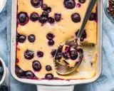 Ein cremiger Quarkauflauf low carb mit Blaubeeren, frisch aus dem Ofen. Eine Löffelportion zeigt die saftige Konsistenz.