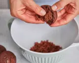 Hände zerbröseln einen Schokoladenkuchen für vegane Desserts. Ein Teil landet in einer weißen Schüssel.