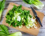 Frischer Pak Choi wird auf einem Holzbrett zerteilt, bereit zum Zubereiten. Ein Messer liegt daneben.