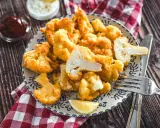 Knusprig panierter Blumenkohl, eine köstliche low carb Alternative zu Pommes. Serviert mit Dips und Zitrone auf einem Holztisch.