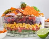 Schichtweise aufgebauter Taco Salat im Glas mit Hackfleisch, Bohnen, Mais, Tomaten, Salat, Nachos, Jalapeños und Avocado.