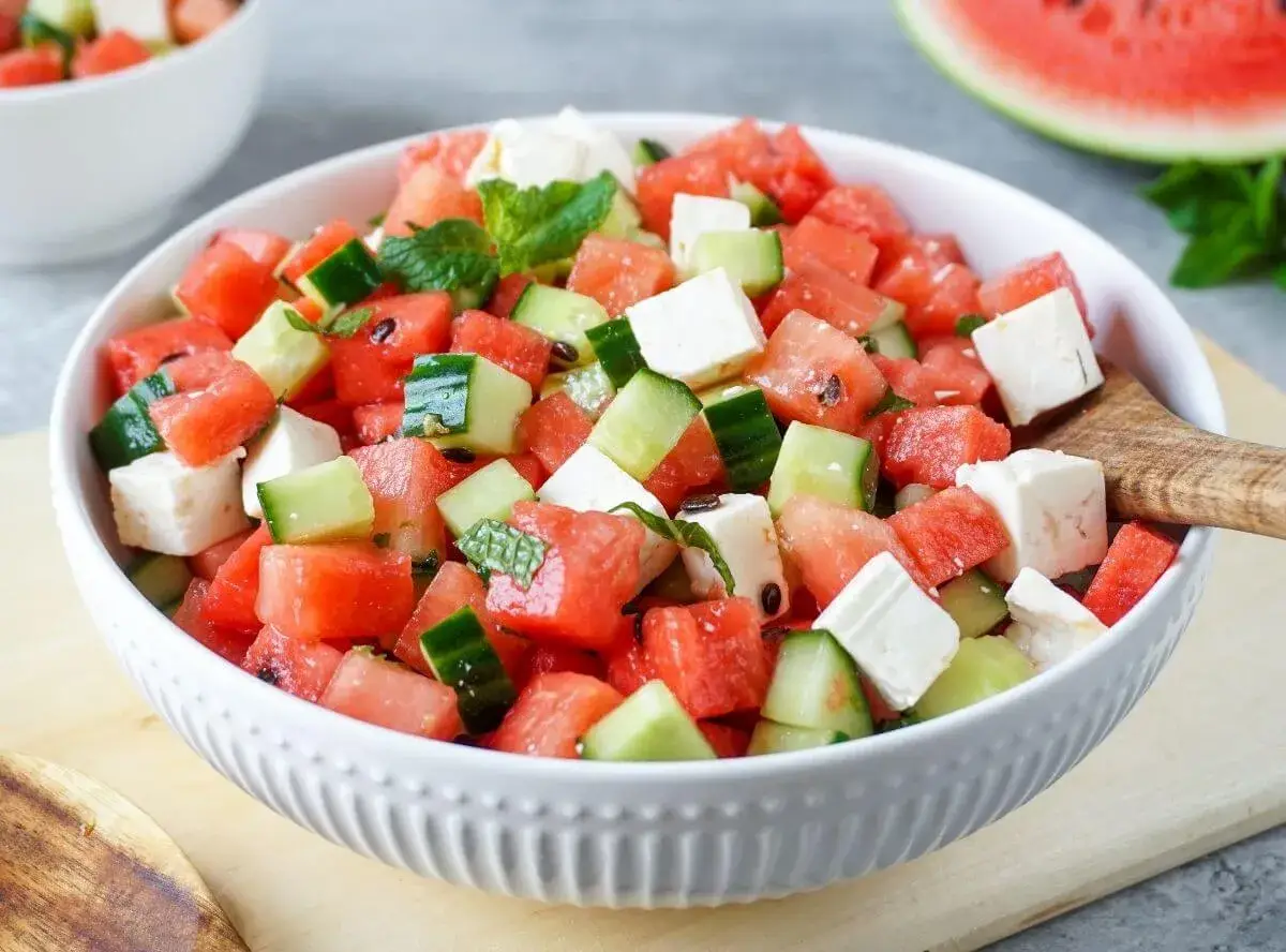 Erfrischender melonen feta salat mit Gurken und Minze in einer weißen Schüssel, bereit zum Servieren.