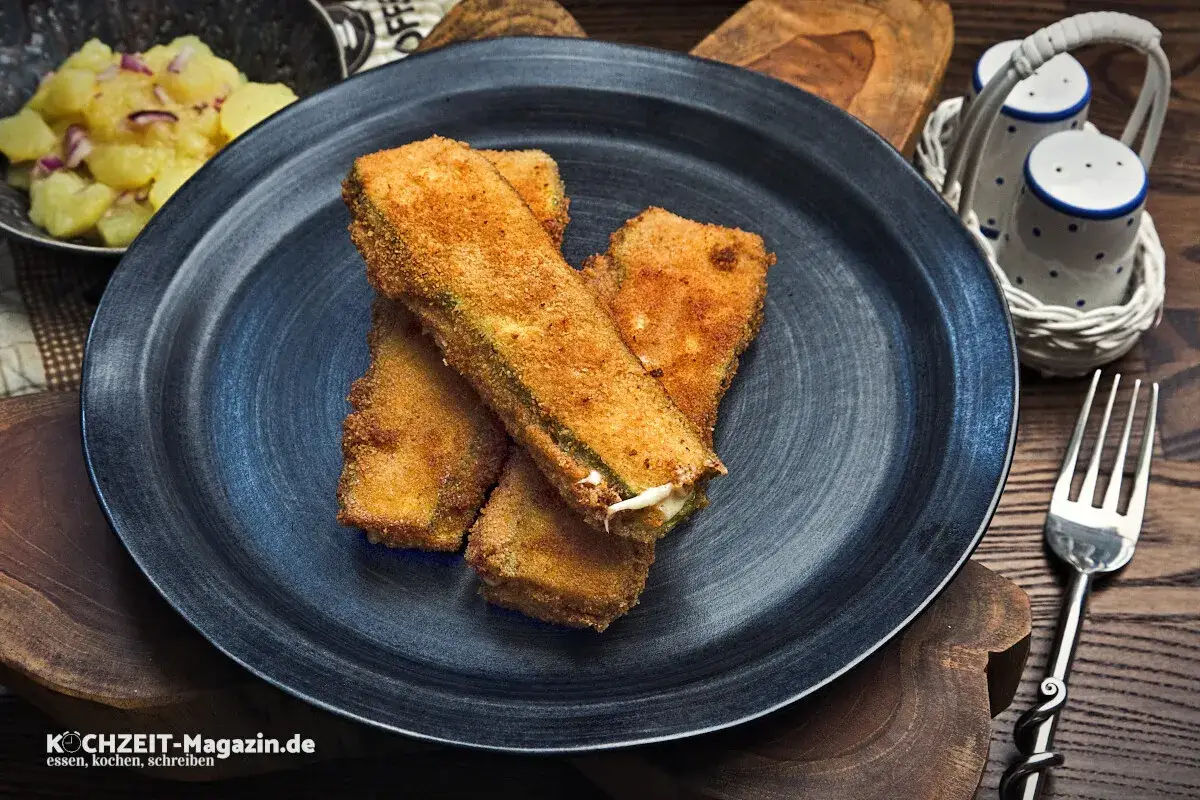 Knusprig panierte Zucchini-Sticks, ein köstliches Gericht, das perfekt zu vielen zucchini rezepte passt. Daneben Kartoffelsalat.
