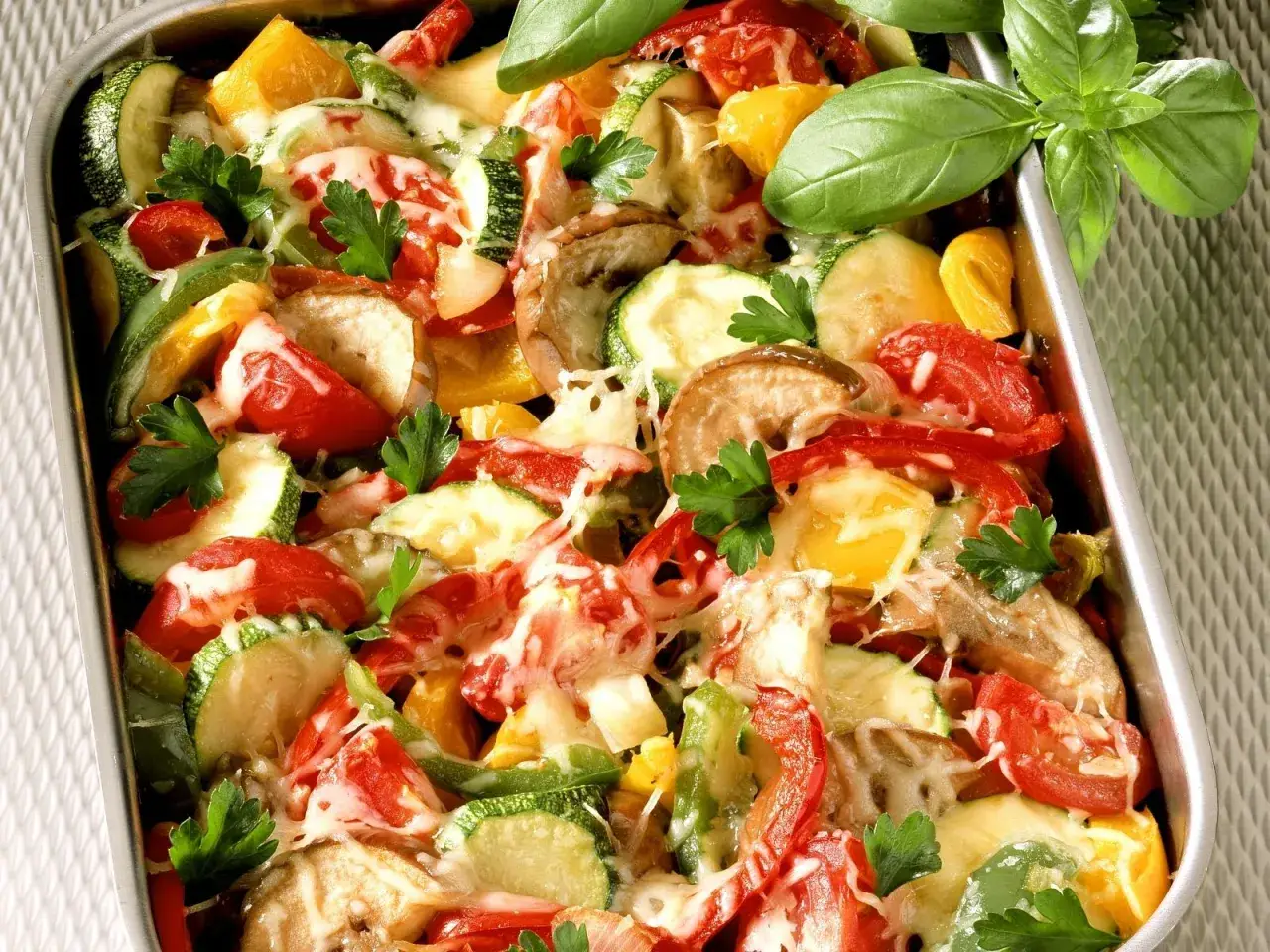 Buntes Ofengemüse mit geschmolzenem Käse, ein köstliches Gericht für low carb rezepte. Frische Kräuter garnieren die Zucchini, Paprika und Tomaten.