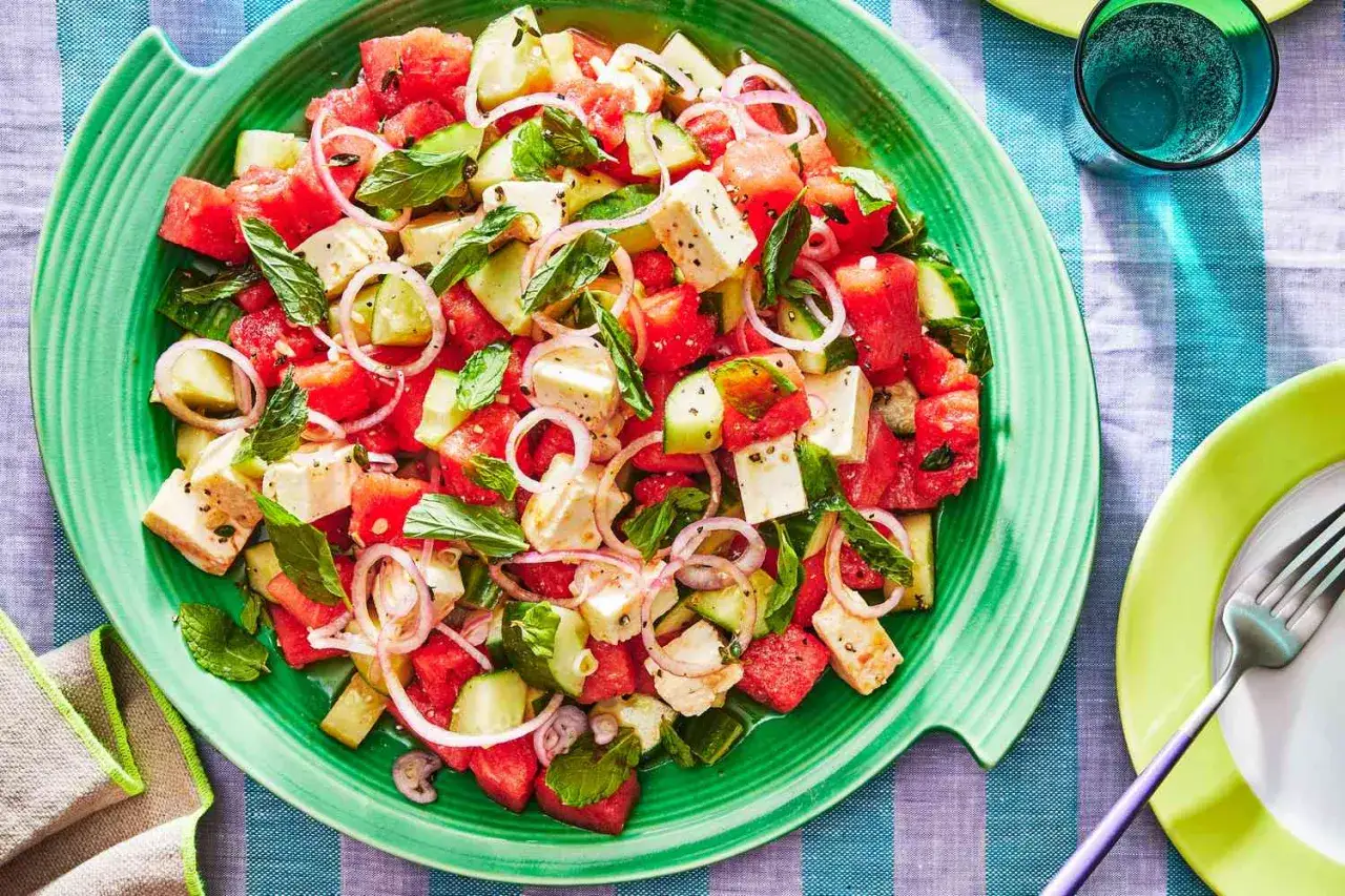 Erfrischender melonen feta salat mit Gurke, roten Zwiebeln und Minze auf einem grünen Teller.