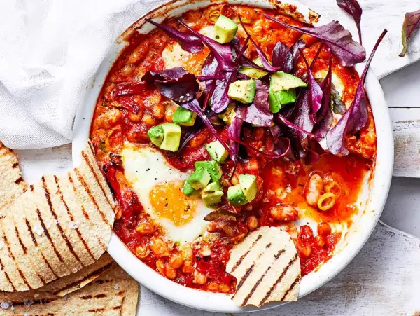 Herzhaftes Gericht mit pochierten Eiern in Tomatensoße, Bohnen, Avocado und Rotkohl. Perfekt für gesunde Rezepte Abendessen. Dazu geröstetes Fladenbrot.