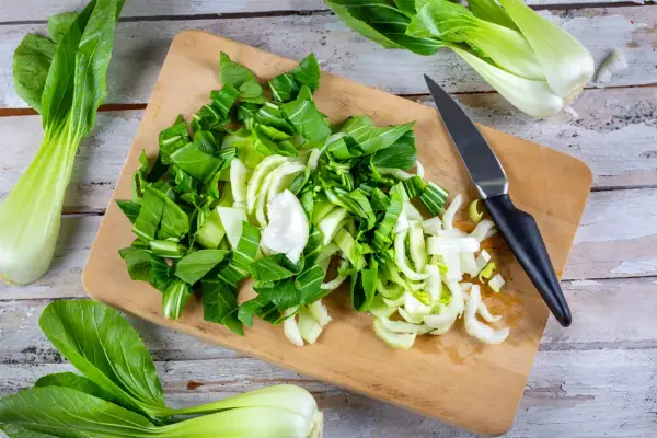 Frischer Pak Choi wird auf einem Holzbrett zerteilt, bereit zum Zubereiten. Ein Messer liegt daneben.