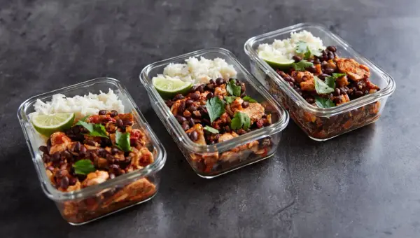 Meal prep für Muskelaufbau: Drei Glasbehälter mit Reis, schwarzen Bohnen, Hähnchen und Limette. Perfekte meal prep muskelaufbau rezepte für deine Fitnessziele.
