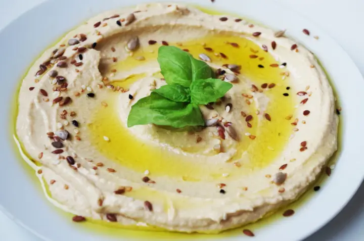 Cremiger Hummus, garniert mit Öl, Kräutern und Samen. Tahin ist die geheime Zutat für diese köstliche Dip-Kreation.